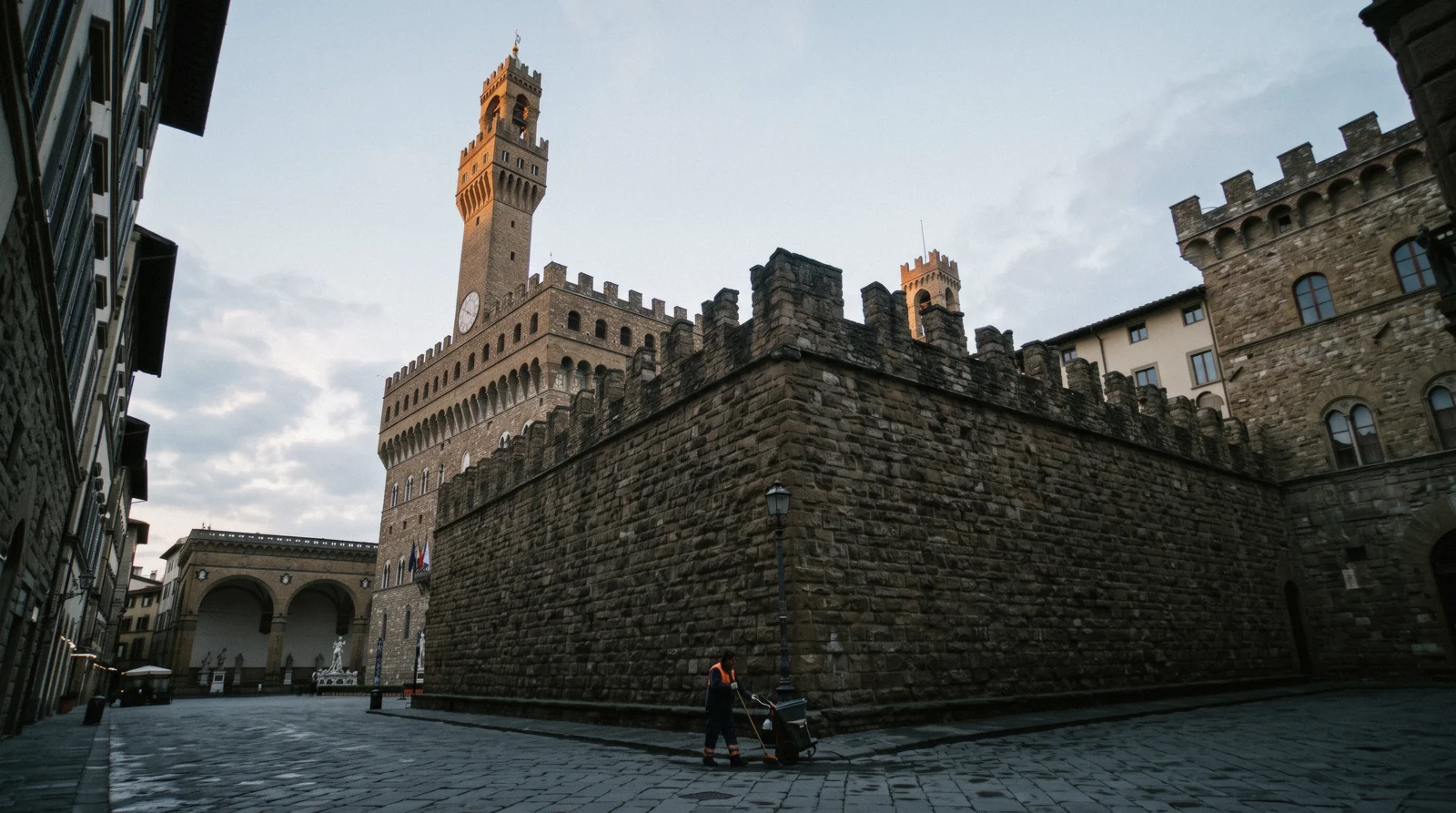 The crenellated facade and clock tower of Palazzo Vecchio in early morning light above an almost empty square, Palazzo Vecchio Florence