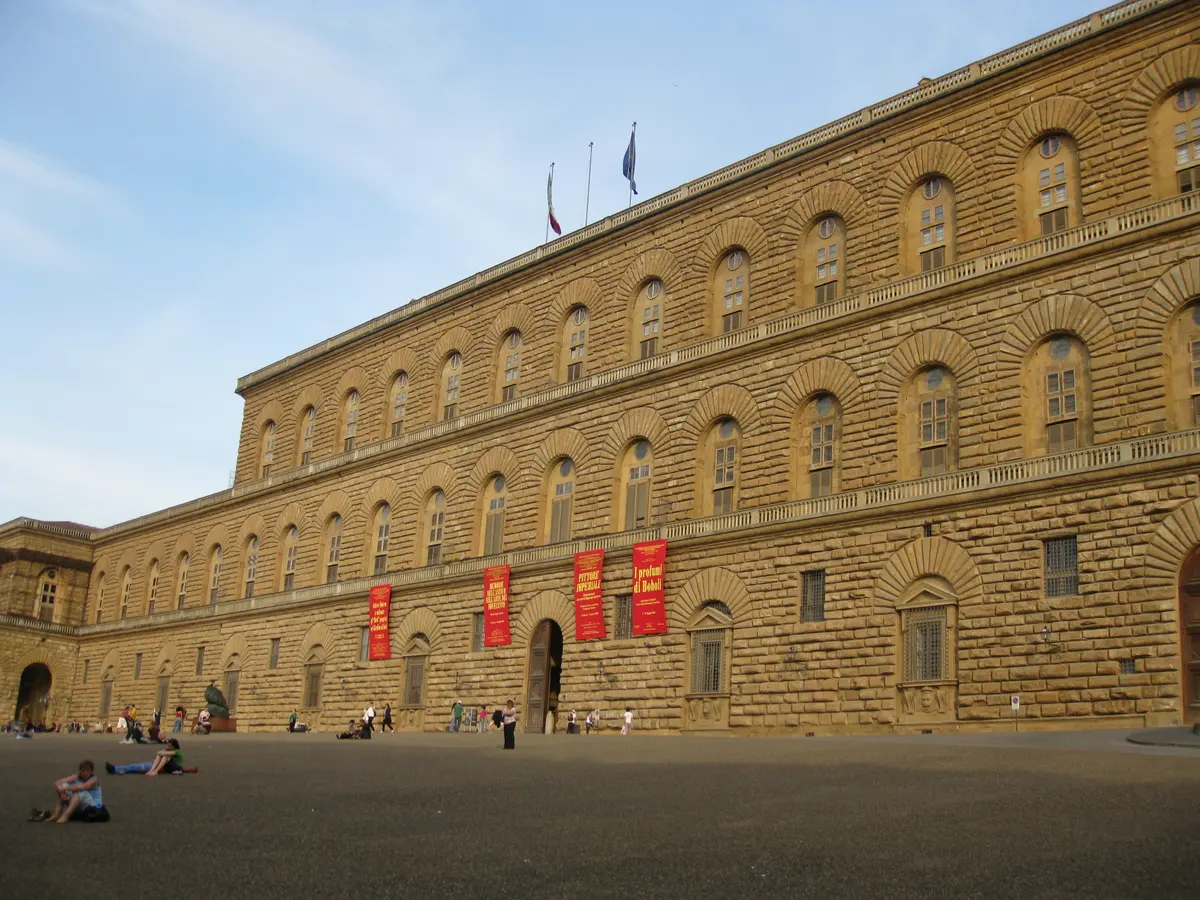 The rusticated stone facade of Pitti Palace across its sloping piazza in late afternoon light
